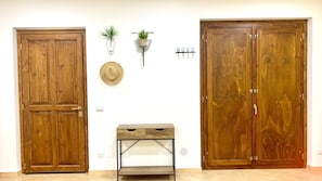 Une pièce avec deux portes en bois, une petite table avec des tiroirs, une étagère murale ornée de plantes et une horloge murale.