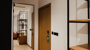 Un pasillo moderno de hotel con piso de madera, una estantería de estructura metálica y una puerta con señal de salida verde de emergencia.