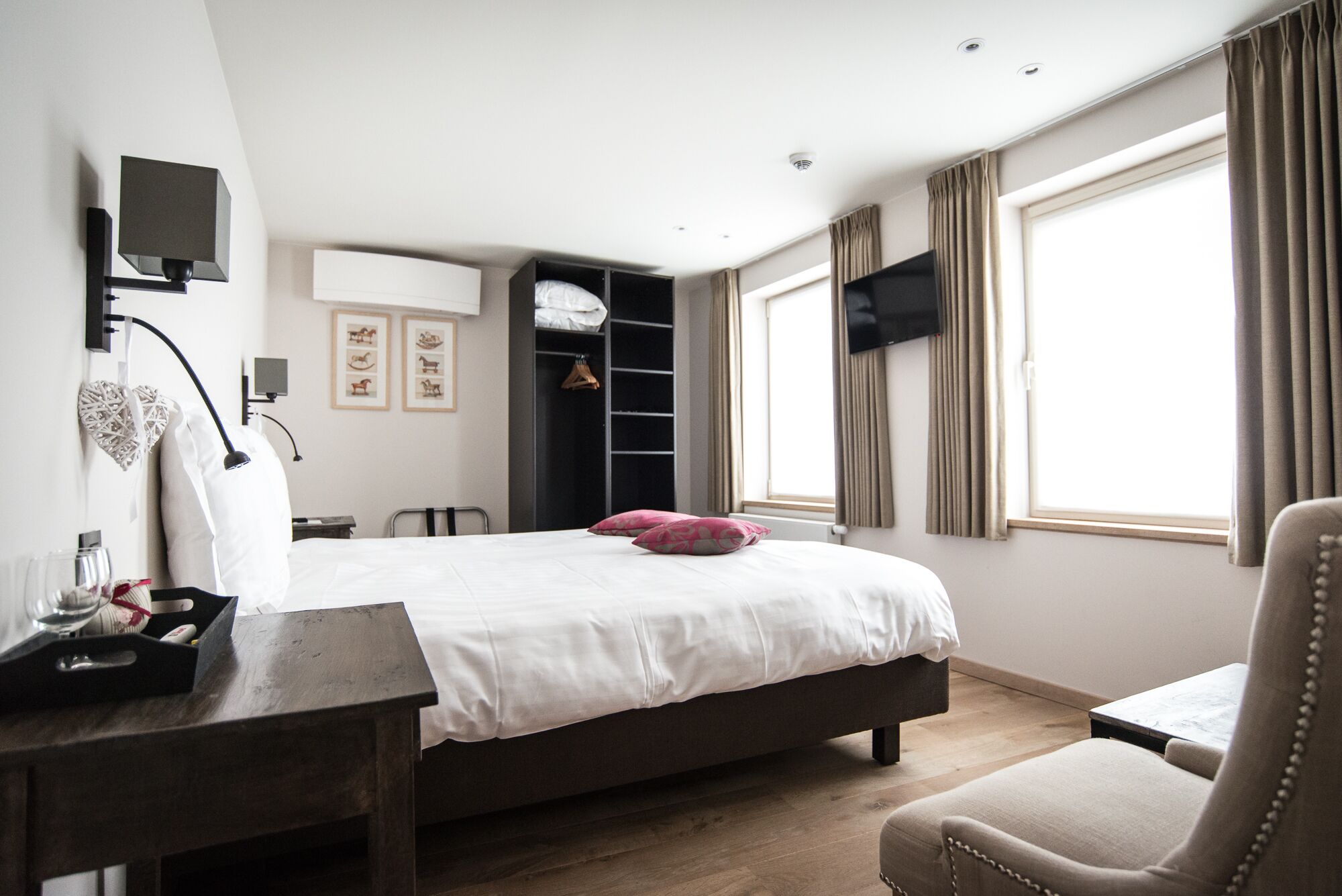 A bedroom with a bed, bedside table, chair, wardrobe, and a TV mounted on the wall.