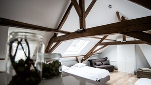 Ein Schlafzimmer im Loft-Stil mit freiliegenden Holzbalken, einem Oberlicht, einem Bett, einem Sessel und einem kleinen Tisch mit einer Pflanzglas.