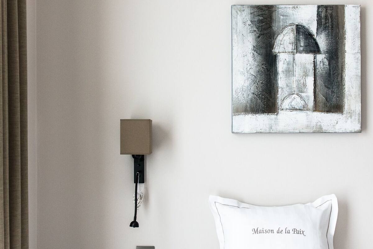 A hotel room with a bed, a nightstand, a lamp, and a painting on the wall.