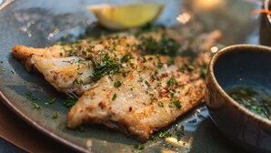 Ein Teller mit einem Fischstück, garniert mit Kräutern und einer Zitronenscheibe, dazu eine Schüssel mit Soße.