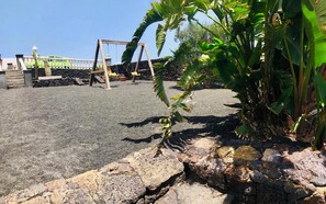 A paved area with a wooden swing set, a stone wall, and a banana plant. - Casita Bellavista with great views in Mozaga (Mozaga)