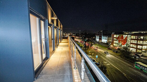 A nighttime view from a balcony overlooking a city street with buildings and a bus lane. - Penthouses in Slough (Slough)