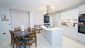 A modern kitchen with white cabinets, a central island, and a dining area with a marble table and wooden chairs. - Penthouses in Slough (Slough)