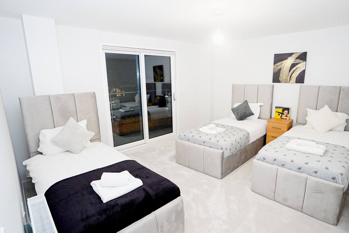 Quarto moderno com duas camas, um sofá pequeno e uma porta de vidro deslizante para uma varanda.