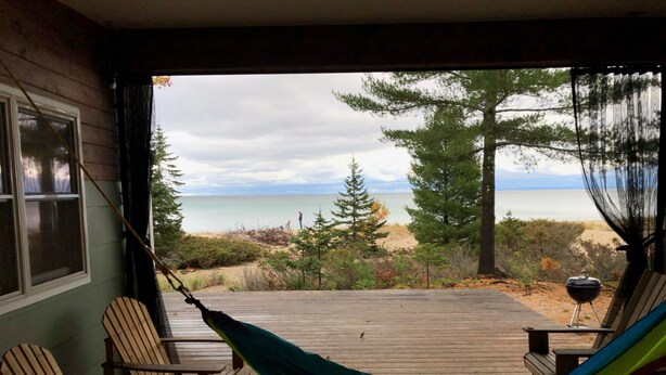 Eine Holzterrasse mit einer Hängematte, Stühlen und Blick auf Strand und Meer.