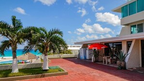 A resort with a pool, palm trees, and a red umbrella. - Ocean Front Roomy Caribbean Condo (Cancún)
