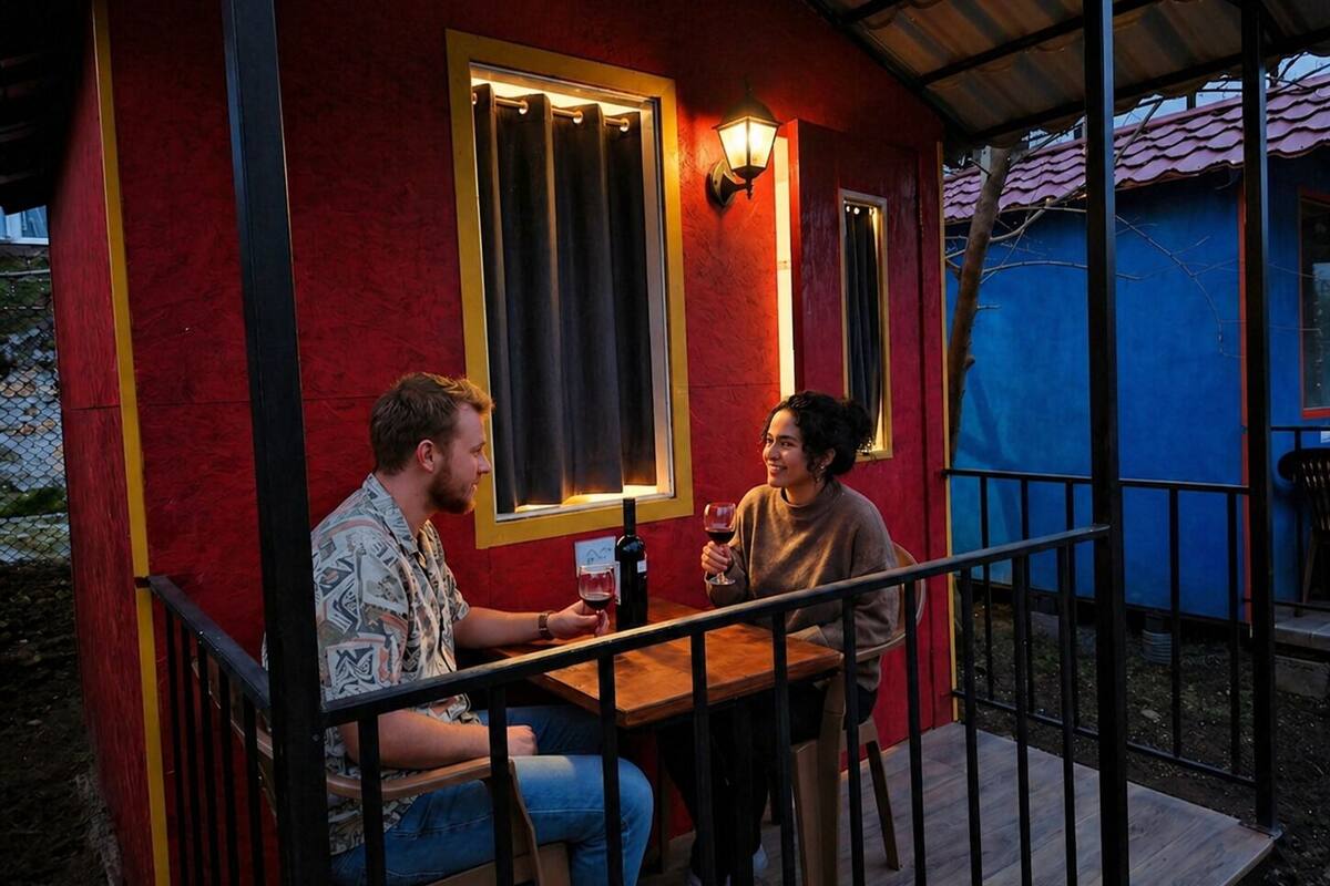 Deux personnes sont assises à une table à l’extérieur, près d’une rambarde, sous une structure dont les murs sont rouges et l’extérieur bleu.