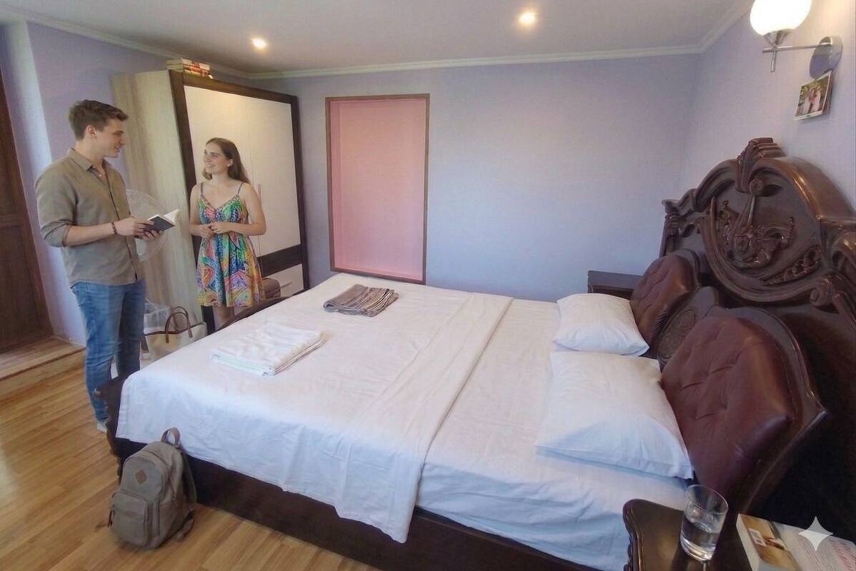Une chambre d’hôtel avec un grand lit, une tête de lit en bois, une table de chevet avec un verre et un miroir.