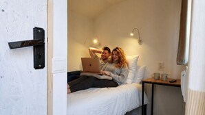 Un dormitorio con una cama, una computadora portátil, un ventilador de techo, una mesita de noche y un pequeño escritorio de madera.