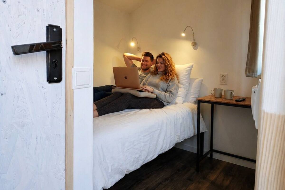 Une chambre à coucher avec un lit, un ordinateur portable, un ventilateur de plafond, une table de chevet et un petit bureau en bois.
