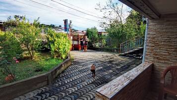 Varanda com parede de pedra, grade de metal e vista para um jardim com um caminho.