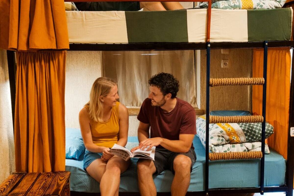 Une chambre avec un lit superposé, un plancher en bois, une petite table en bois et des rideaux orange.