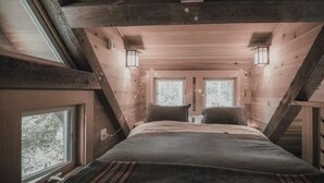 Ein gemütliches Schlafzimmer im Dachgeschoss mit einem Bett, zwei Fenstern und Lichterketten.