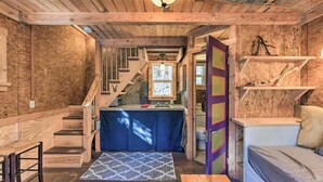 Ein rustikales Blockhaus-Interieur mit einer Holztreppe, einer kleinen Küchenzeile, einem Bett und einer farbenfrohen Tür.