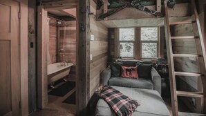 Ein rustikales Blockhaus-Interieur mit Schlafkoje, kleinem Fenster und einer Leiter.