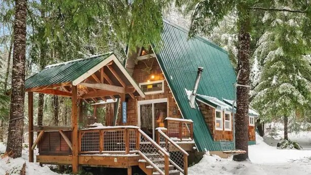 Eine Holzhütte mit steilem Dach, umgeben von Schnee und Bäumen.