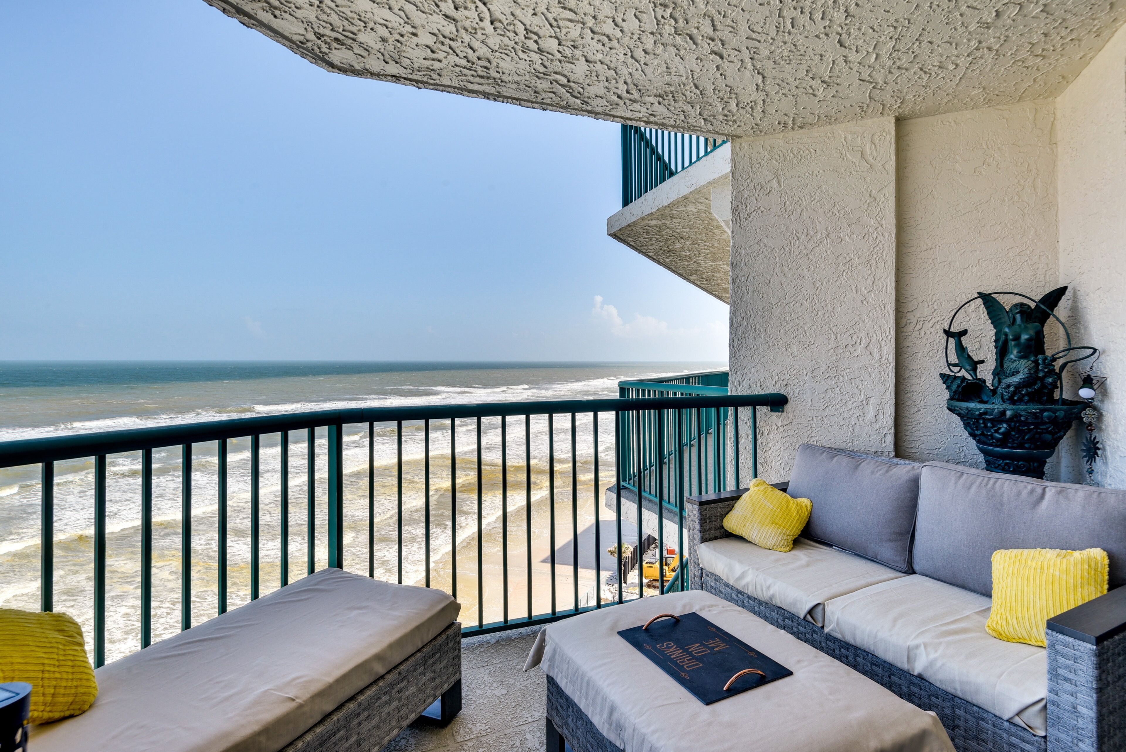 A balcony with a view of the ocean, a sofa with cushions, and a decorative planter.