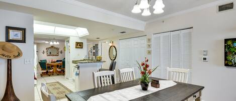 A dining area with a wooden table, white chairs, a vase with flowers, and a chandelier.