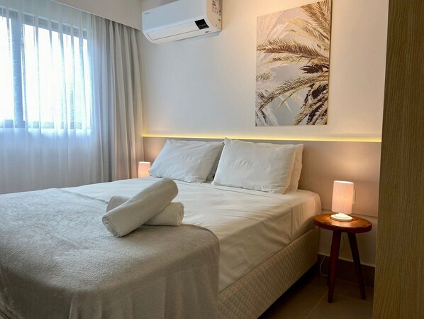 A neatly made bed with white linens and a folded towel, a bedside lamp, and a wall-mounted air conditioner. - Green Porto 105 (Ipojuca)
