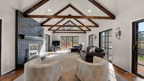 Un salón espacioso con chimenea, ventanas amplias y un techo alto con vigas a la vista.