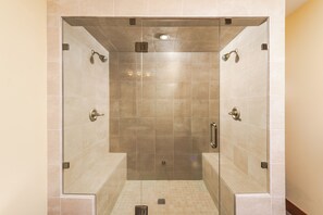 A glass-enclosed walk-in shower with a tiled floor and walls, a handheld showerhead, and a control panel.