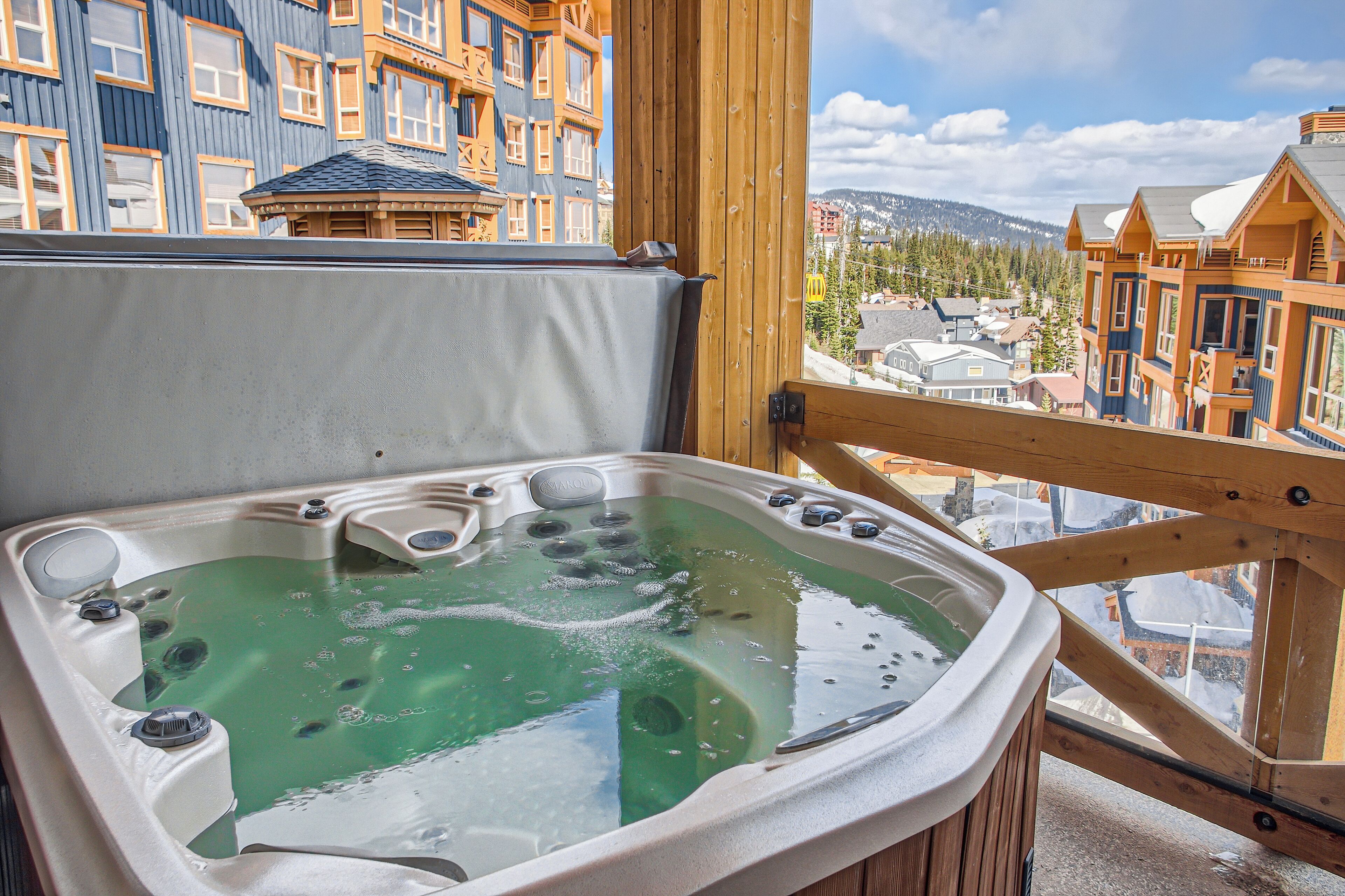 A hot tub with a wooden deck and a view of a mountain town.