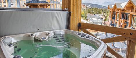 A hot tub with a wooden deck and a view of a mountain town.