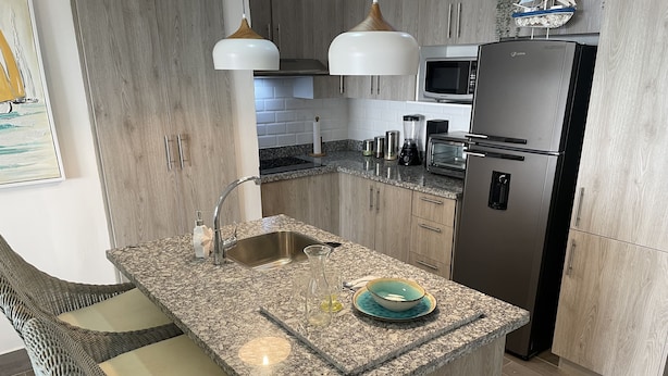 A modern kitchen with a granite countertop, stainless steel appliances, and a built-in island with seating. - Coral Criff juan dolio (Guayacanes)