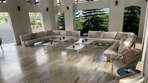 A spacious lounge area with a sectional sofa, multiple small tables, and wicker chairs. - Coral Criff juan dolio (Guayacanes)