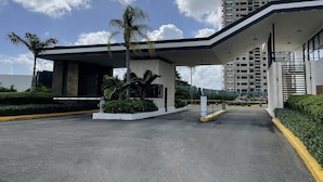A modern building with a covered entrance, palm trees, and a clear sky. - Coral Criff juan dolio (Guayacanes)