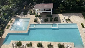 An aerial view of a resort with a large rectangular pool, sun loungers, and a children's play area. - Coral Criff juan dolio (Guayacanes)