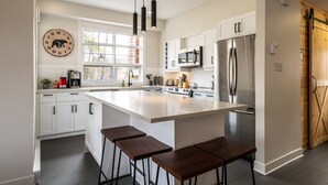 Een moderne keuken met witte kasten, een groot eiland met barstoelen, roestvrijstalen apparatuur en een klok aan de muur.