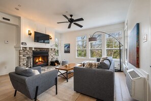 Ein Wohnzimmer mit Kamin, grauen Sofas, einem Couchtisch und einem Fernseher, der über dem Kamin angebracht ist.