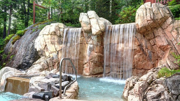Een natuurlijk rotsbad met een waterval, omringd door groen.