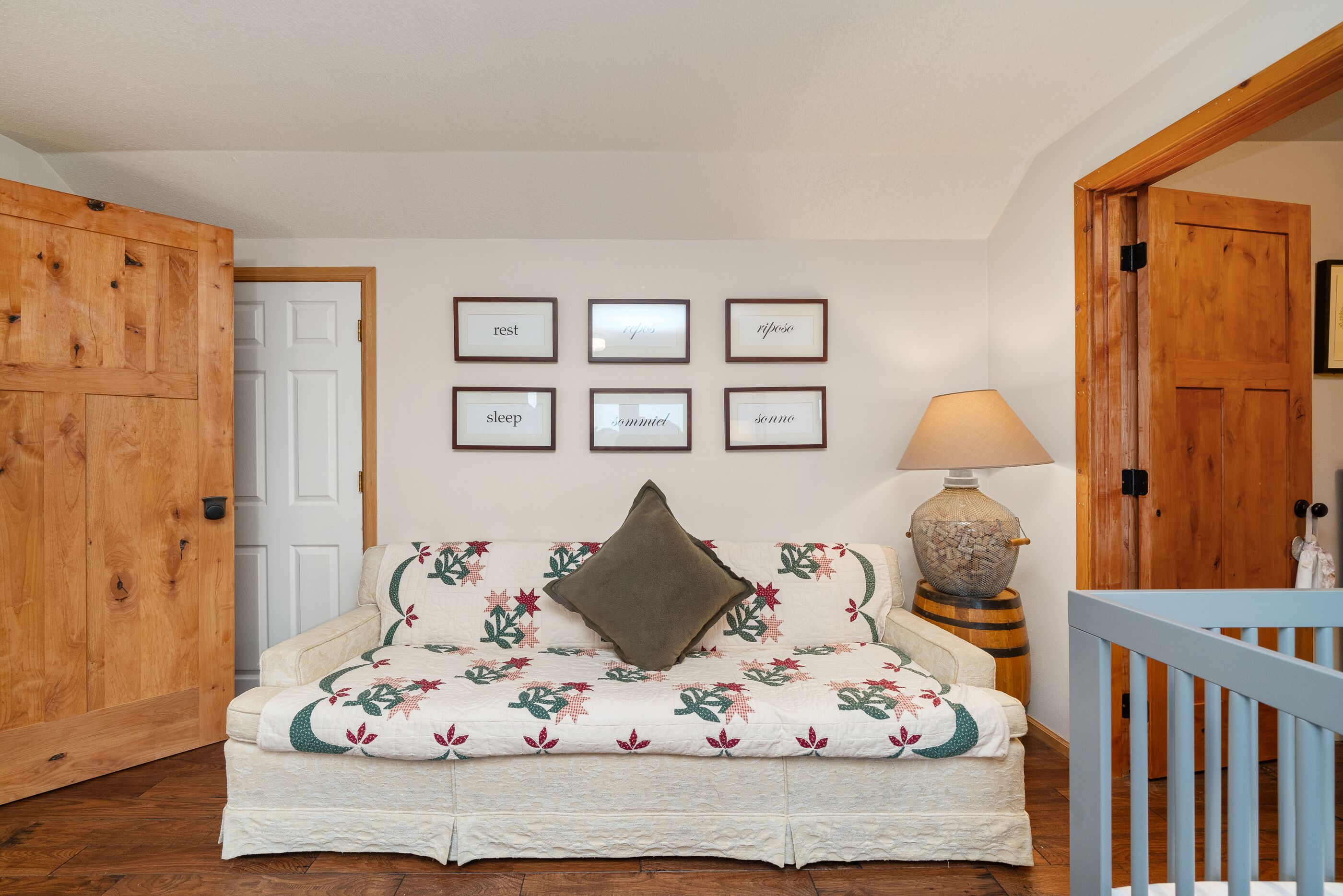 A cozy room with a wooden door, a white wall with framed inspirational words, a floral sofa, and a lamp.