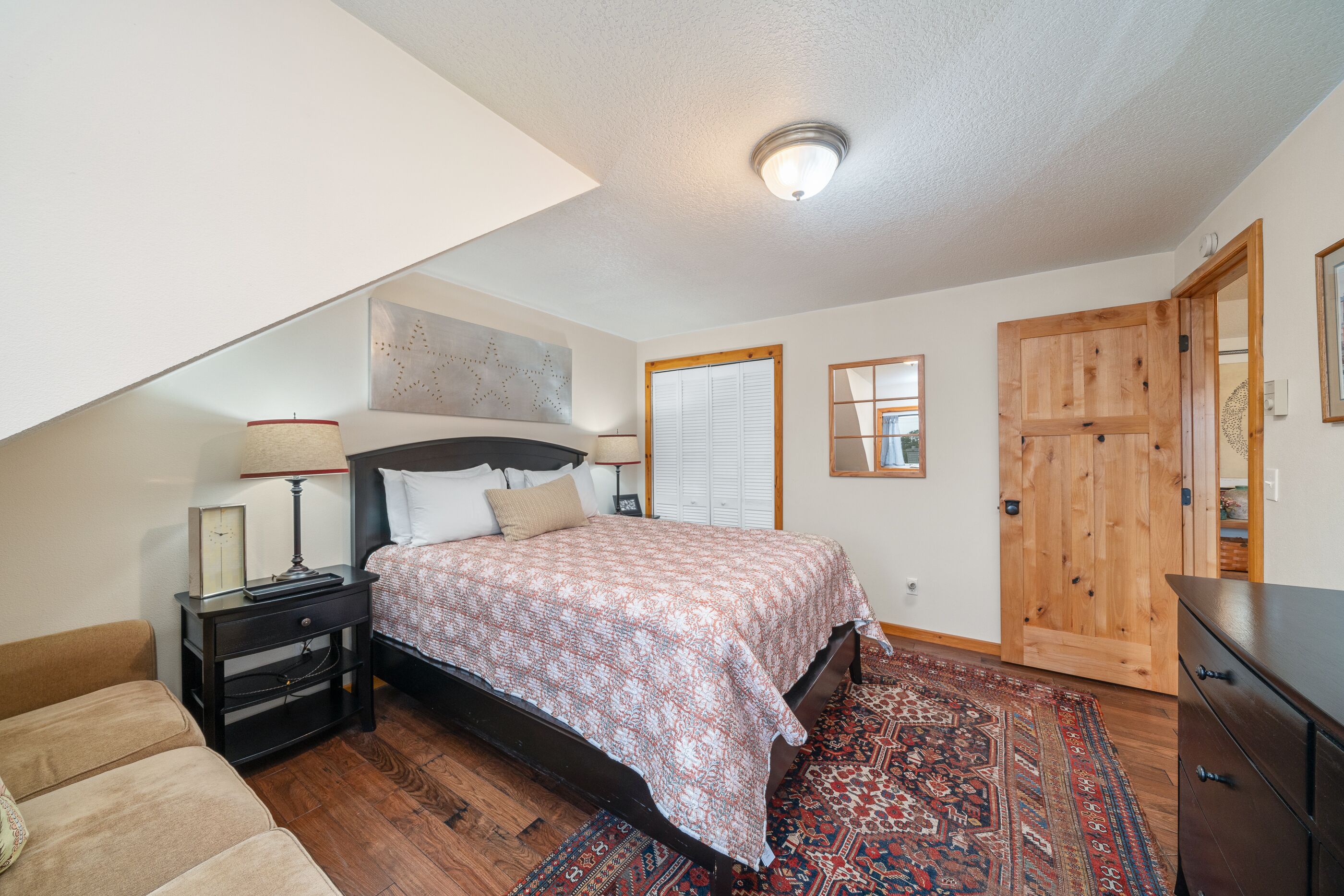 A bedroom with a bed, nightstand, dresser, and a large window.