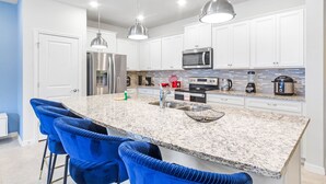 A modern kitchen with white cabinets, a granite countertop, stainless steel appliances, and blue bar stools. - Relaxing 5 Bed Townhome with Splash Pool-3966LA (Davenport)
