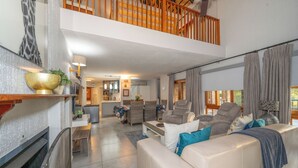 A spacious living area with a high ceiling, a fireplace, and a dining area with wicker furniture. - Kruger Park Lodge Unit No. 205 (Mbombela)
