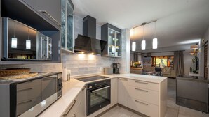 A modern kitchen with a built-in oven, a microwave, and a stove. There is a large island with a sink and a refrigerator. The kitchen has a large window and a view of the outside. - Kruger Park Lodge Unit No. 205 (Mbombela)