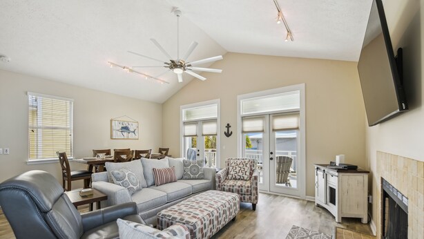 A spacious living room with a gray sectional sofa, a patterned ottoman, a leather armchair, and a ceiling fan.