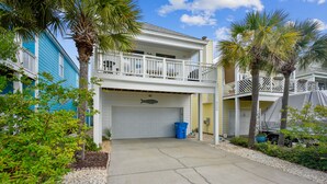 A two-story house with a balcony, a garage, and a small garden area with palm trees.