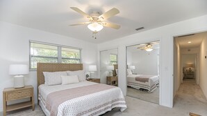 A bedroom with a large bed, a ceiling fan, bedside tables with lamps, a mirror, and a view of a hallway. - Beachside Bliss in The Moorings | 3BR Naples Stay (Naples)