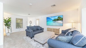 A modern living room with a grey sofa, a beige ottoman, and a large flat-screen TV on the wall. - Beachside Bliss in The Moorings | 3BR Naples Stay (Naples)