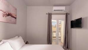 A hotel room with a bed, a flat-screen TV, an air conditioning unit, and a view of the outside through a sliding door.