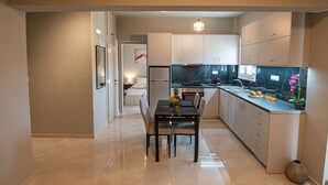 A modern kitchen with a marble countertop, white cabinets, and a dining area with a table and chairs.