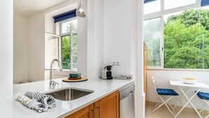 A modern kitchen with a built-in dishwasher, a window with a view of greenery, and a small dining area with a table and chairs.