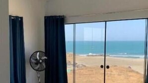 A bedroom with a bed, a fan, and a view of the beach. - Deluxe Double Room with Balcony and Sea View (Pis Lobitos)