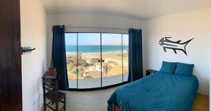 Enjoy a serene beach view from the large bay window in this inviting room, featuring a comfortable bed and a potted plant.